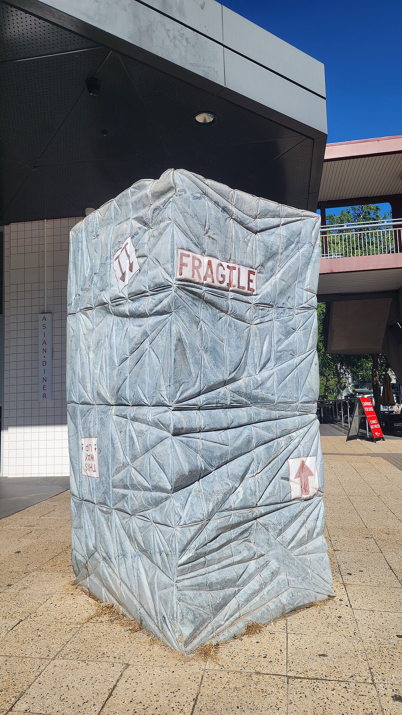 A large marble sculpture carved to resemble a tightly wrapped parcel, with fragile labels and cord inlays.