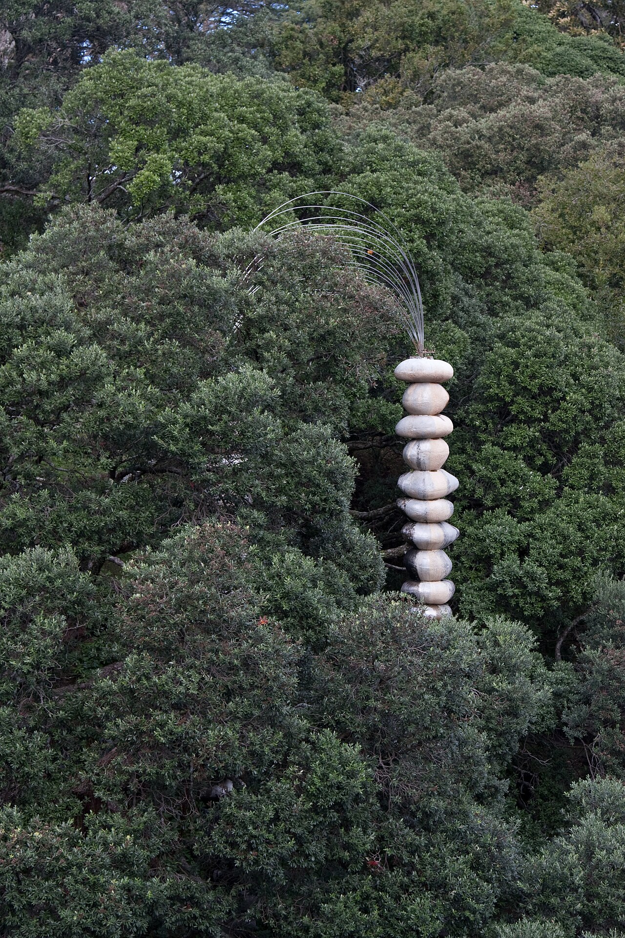 A pillar of rounded basalt boulders topped by an arch of metal rods, among trees in Albert Park, Auckland.