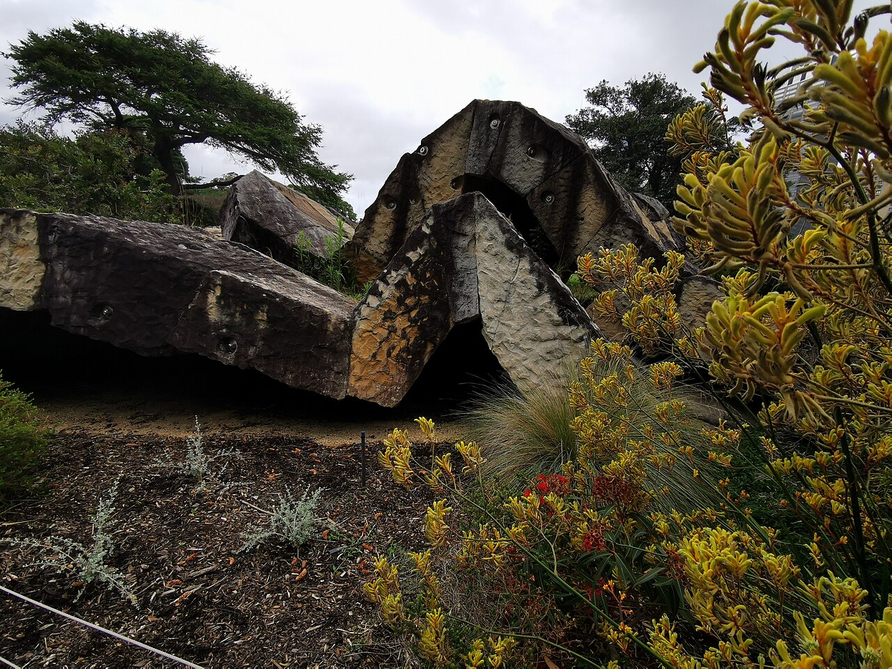 Massive sandstone blocks form a folded wave among native plants in the Royal Botanic Garden, Sydney.