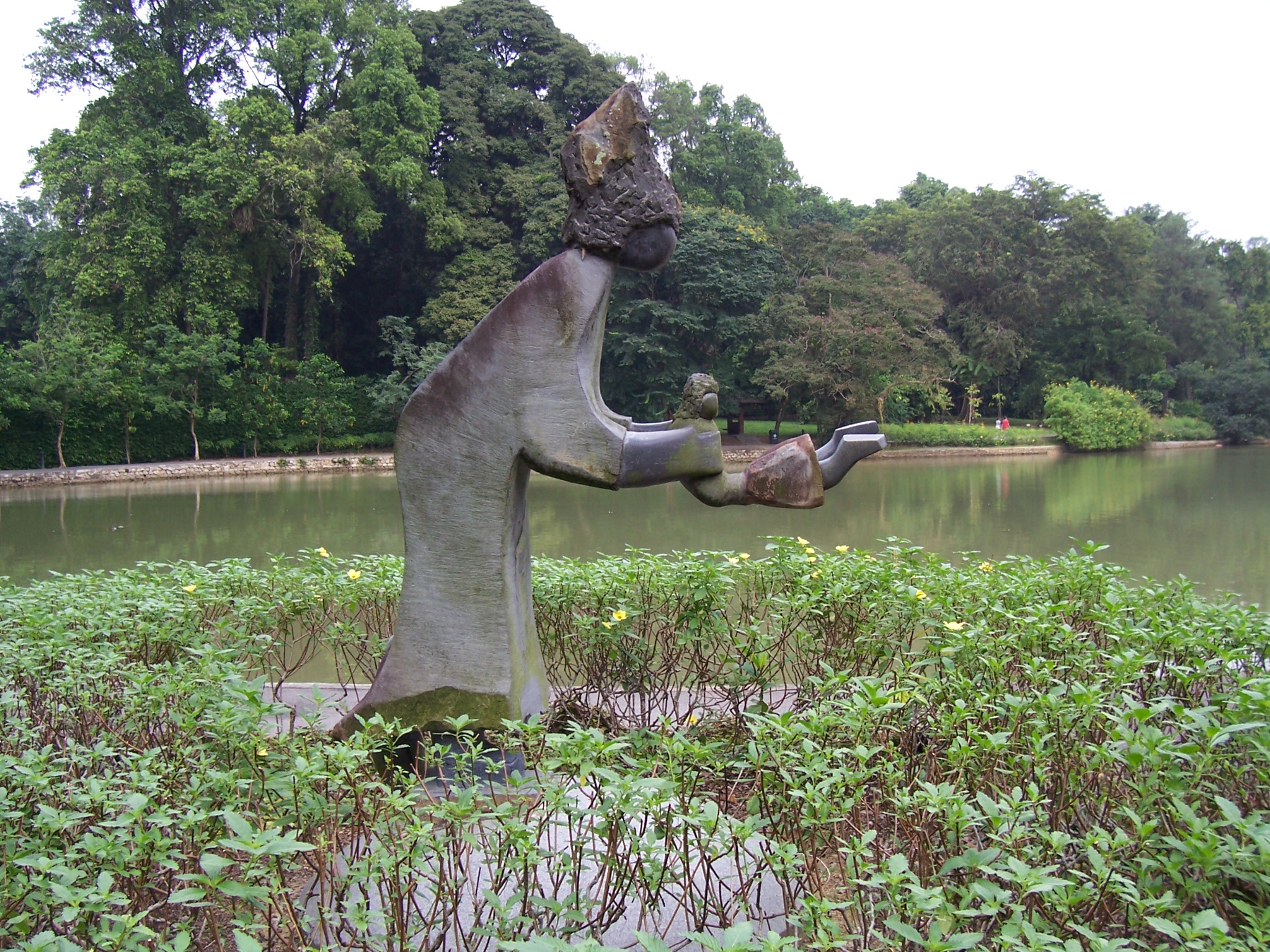 Dominic Benhura’s dark stone sculpture of a mother swinging her child, installed beside a path in Singapore Botanic Gardens.