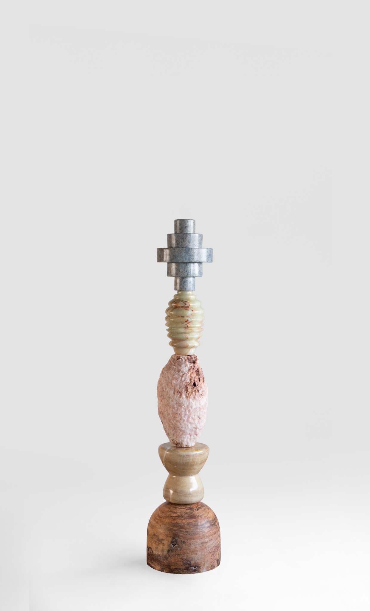 A vertical stone sculpture combining grey calcite, ribbed yellow onyx, and textured pink and brown stone