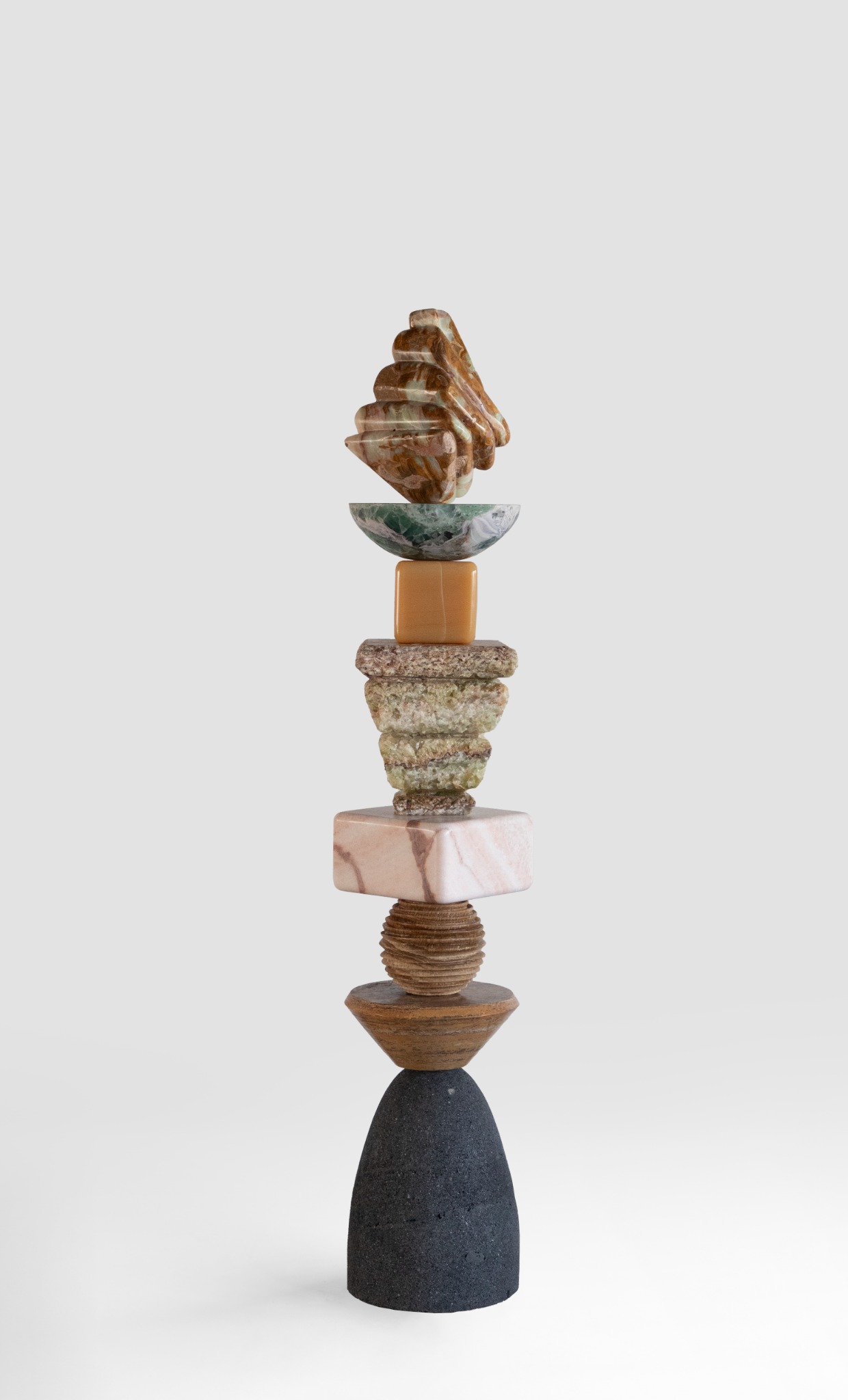 A tall totem of varied stone forms, with a dark rounded base, textured middle sections, and a carved amber-coloured top