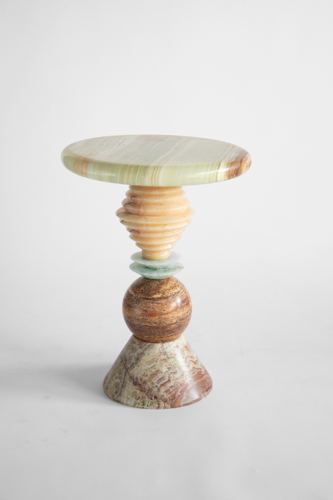 A stone side table with a pale green circular top, a ribbed amber stem, and a patterned stone base