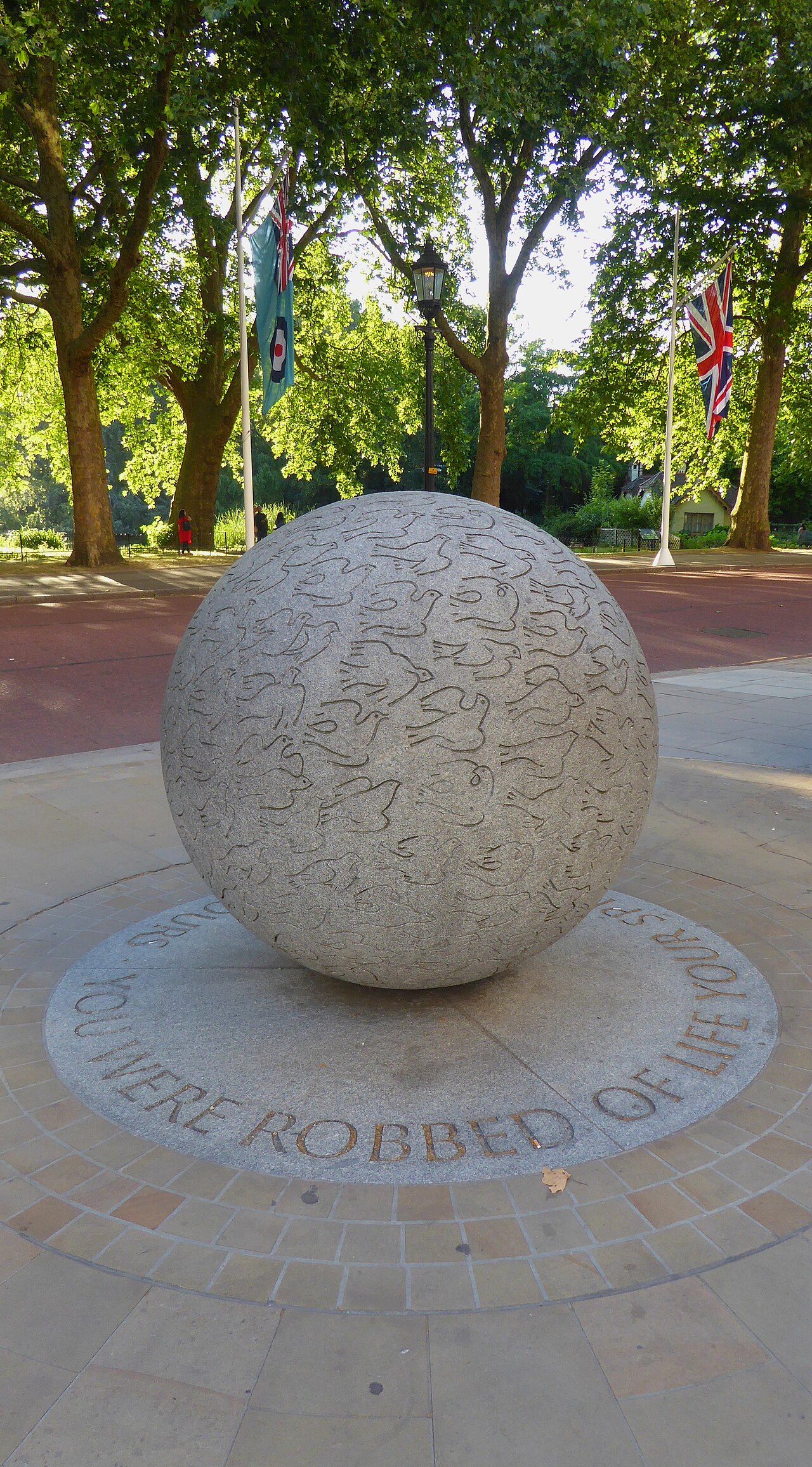 A granite globe carved with doves above the pale stone wall of the Bali Bombings Memorial in London.