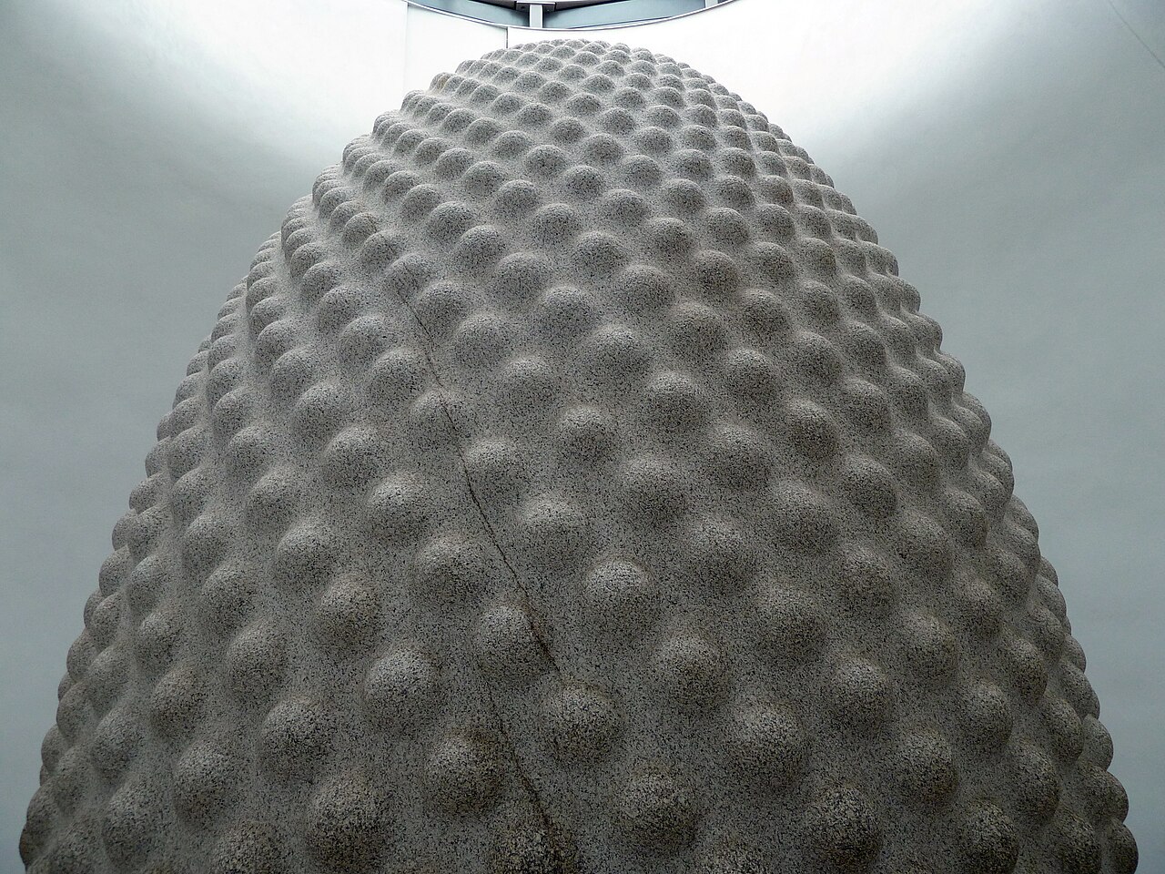 A large granite Seed sculpture, its curved surface covered with interlocking carved forms, inside the Eden Project.